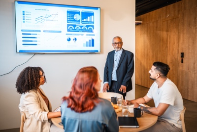 Senior Multiracial Male Project Manager Presenting Financial Report to Diverse Colleagues
